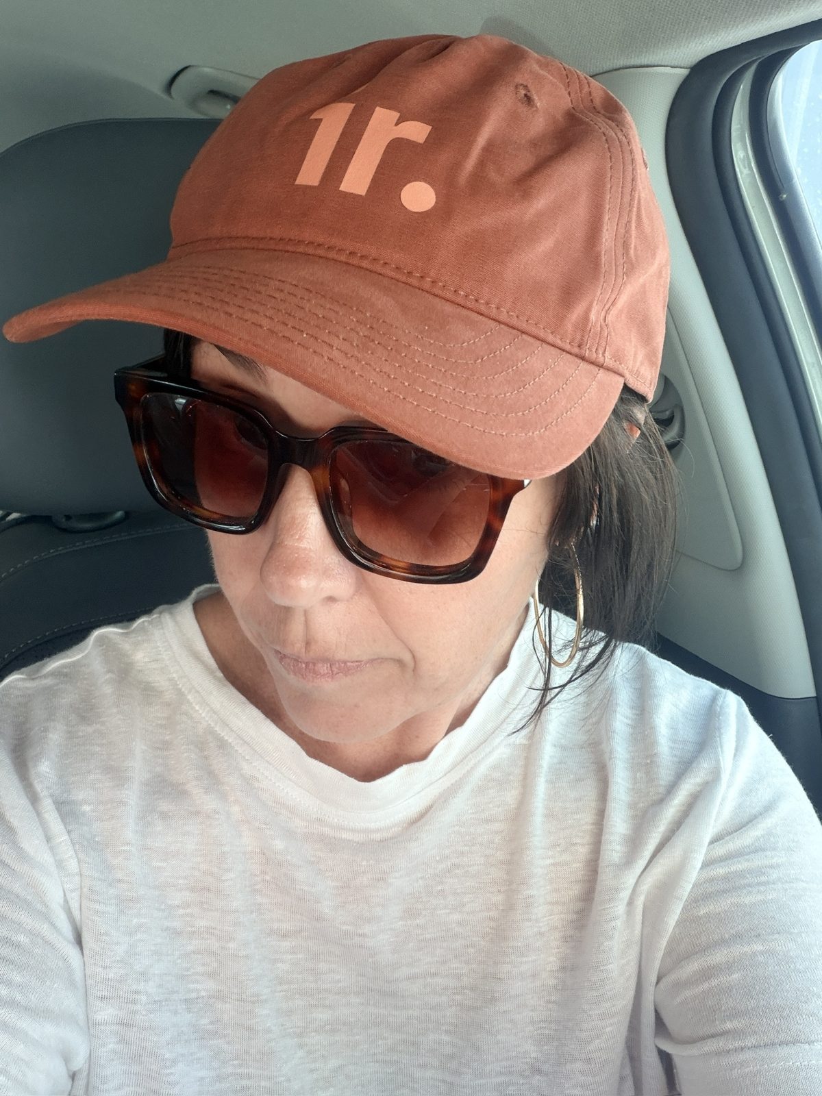 Karla in a cap and sunglasses, filming a selfie in the driver's seat